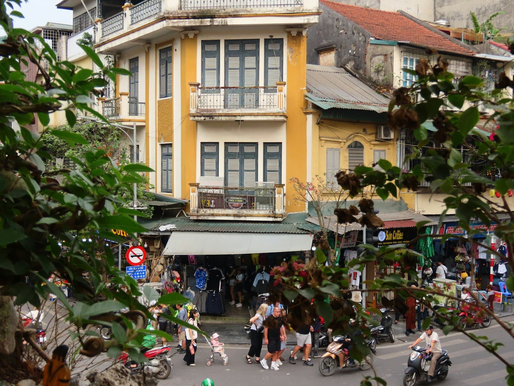 Everyday Hanoi Old Quarter street with mustard-yellow shophouses, scooters, and shopfronts