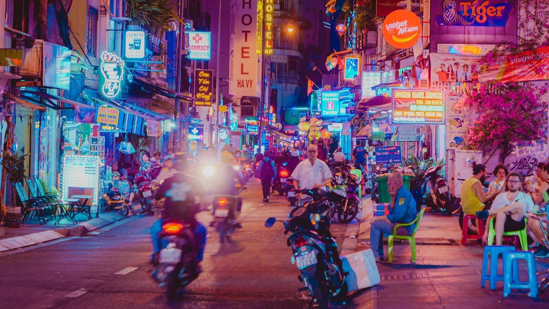Night street in Ho Chi Minh City with neon signs, motorbikes, and sidewalk stalls