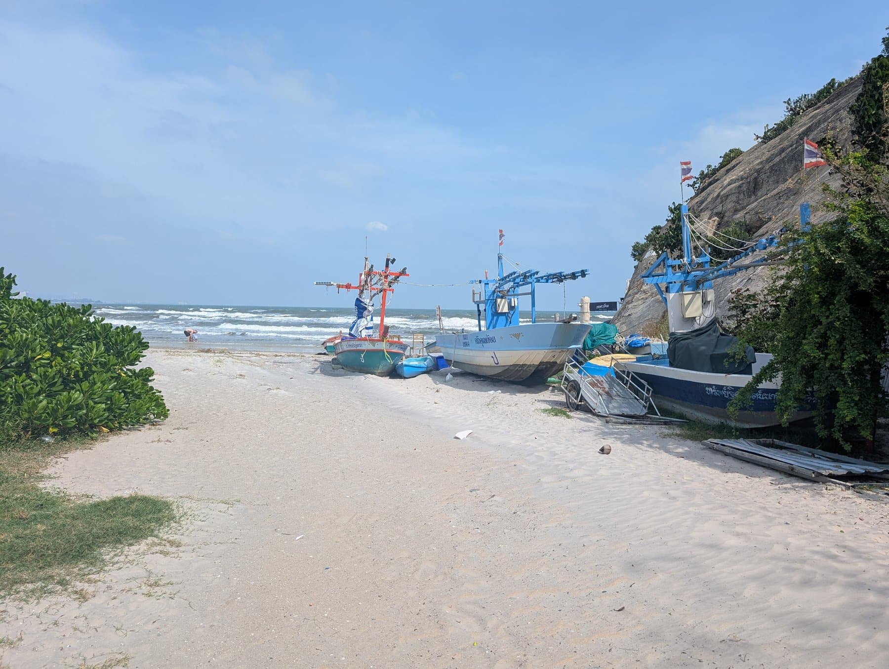 Fishing boats on Hua Hin beach beside a rocky headland, photographed in November 2024